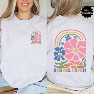 May include: A grey unisex sweatshirt with a rainbow and flower design. The text "SCHOOL PSYCH" is printed on the front and back of the sweatshirt.