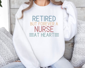 May include: White sweatshirt with the text "Retired but forever a nurse at heart" in colorful lettering.