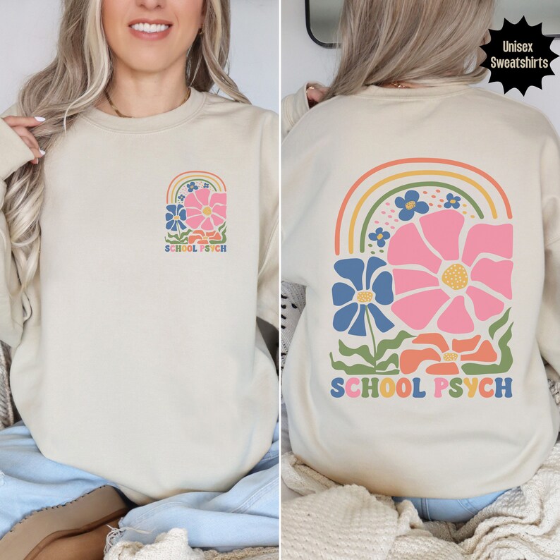 May include: A beige sweatshirt featuring a rainbow and flower design. The text "SCHOOL PSYCH" is printed on the front and back of the sweatshirt.