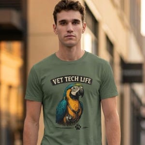 Può includere: T-shirt verde oliva con la scritta "VET TECH LIFE" e un pappagallo con uno stetoscopio. Il pappagallo è blu, giallo e nero. La persona indossa pantaloni blu navy e scarpe da ginnastica bianche.