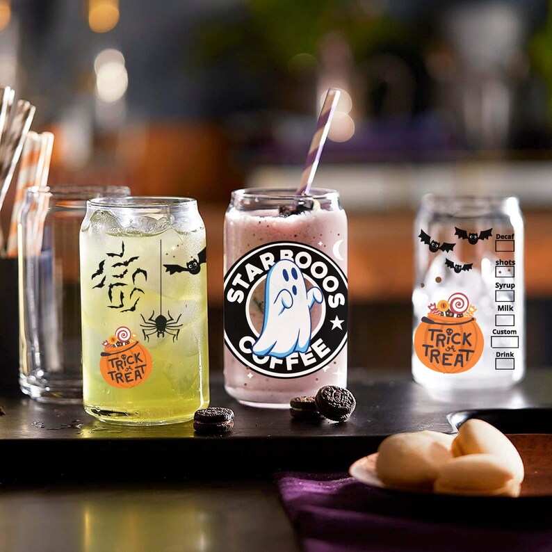 May include: Three clear glass cups with Halloween-themed designs. The cup on the left has a spider and the text "Trick or Treat". The middle cup has a ghost and the text "Starbucks Coffee". The cup on the right has a pumpkin and the text "Trick or Treat".