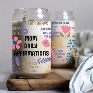 K&ouml;nnte beinhalten: Ein Glasgef&auml;&szlig; mit wei&szlig;em Hintergrund und bunten Blumenmustern. Das Gef&auml;&szlig; tr&auml;gt den Text "Mom Daily Affirmations" und enth&auml;lt S&auml;tze wie "Ich bin mutig", "Ich verdiene es, mich auszuruhen" und "Um Hilfe zu bitten, macht mich stark".