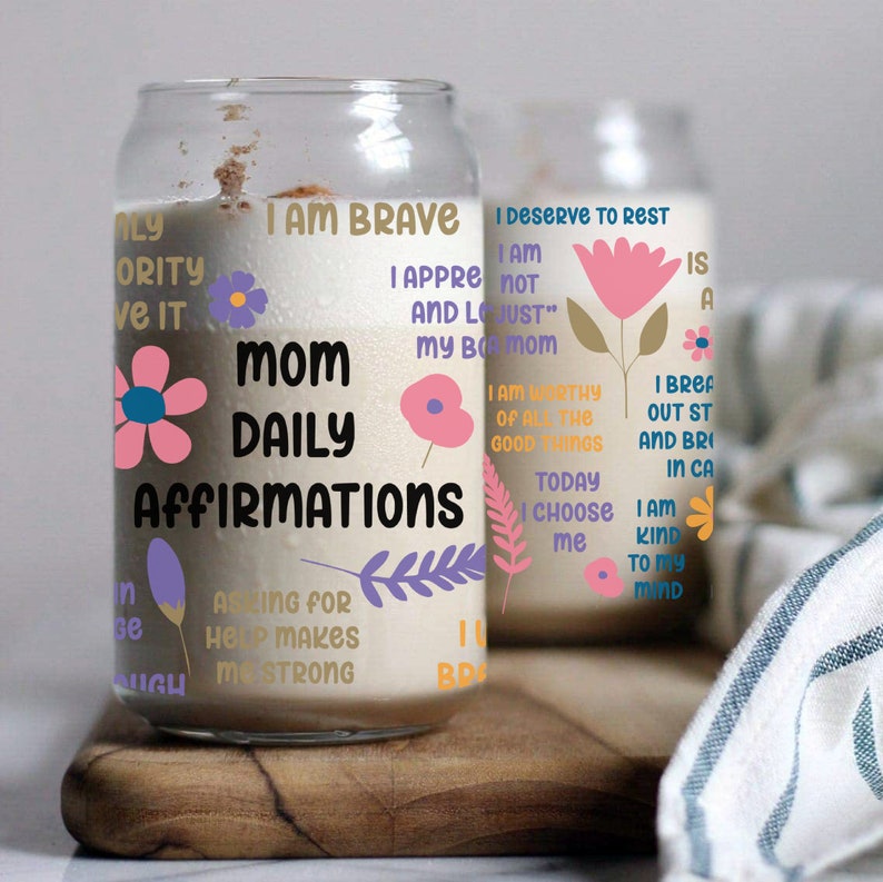 K&ouml;nnte beinhalten: Ein Glasgef&auml;&szlig; mit wei&szlig;em Hintergrund und bunten Blumenmustern. Das Gef&auml;&szlig; tr&auml;gt den Text "Mom Daily Affirmations" und enth&auml;lt S&auml;tze wie "Ich bin mutig", "Ich verdiene es, mich auszuruhen" und "Um Hilfe zu bitten, macht mich stark".