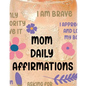 K&ouml;nnte beinhalten: Eine durchsichtige Glasdose mit einer rosa Grapefruit-Scheibe oben drauf. Die Dose hat ein florales Design und einen Text, der "Mom Daily Affirmations" lautet und S&auml;tze wie "Ich bin mutig", "Hilfe zu bitten macht mich stark" und "Ich sch&auml;tze und liebe meinen K&ouml;rper" enth&auml;lt.
