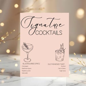 Puede incluir: Un letrero rosa con la frase "Signature Cocktails" en cursiva. Muestra ilustraciones de dos cócteles con ingredientes: Blushing Bride Spritz y Old Fashioned Twist. El letrero está sobre una superficie de mármol.