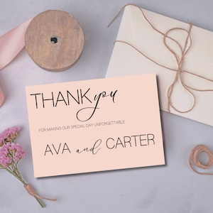 Puede incluir: Una tarjeta de agradecimiento rosa pálido con las palabras "THANK you" en una fuente elegante. La tarjeta también dice "FOR MAKING OUR SPECIAL DAY UNFORGETTABLE" y "AVA and CARTER". Una bobina de madera, una cinta rosa y un ramo de flores secas también están en la imagen.