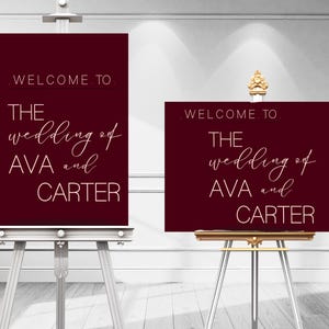 May include: Two burgundy wedding signs with gold lettering that read "WELCOME TO THE wedding of AVA and CARTER." The signs are displayed on silver easels. One sign is rectangular, the other is square.