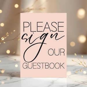 Puede incluir: Un letrero rectangular con el texto "PLEASE sign OUR GUESTBOOK" en letras negras sobre un fondo rosa claro. La palabra "sign" está escrita en cursiva. El letrero es probablemente para una boda o evento.