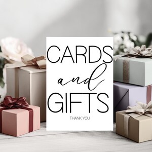 May include: A white sign with the words "CARDS and GIFTS" in black script, with "THANK YOU" below. The sign is surrounded by wrapped gift boxes in various colors, including pink, green, and tan, with ribbon bows.