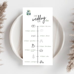 May include: A white wedding day schedule card with the words "our wedding day" in a stylish script. The timeline lists events like vows, photos, dinner, speeches, first dance, evening food, cake, and carriages. Eucalyptus and line drawings decorate the card.