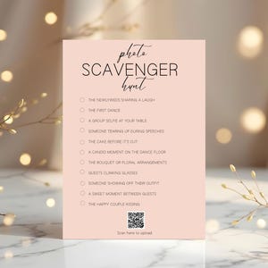 Könnte beinhalten: Eine blassrosa Hochzeits-Foto-Schnitzeljagdkarte mit einer Liste von Aufforderungen. Die Karte zeigt die Worte "Foto-Schnitzeljagd" in einer handschriftlichen Schriftart. Die Liste enthält Aufforderungen wie "Der erste Tanz" und "Das glückliche Paar küsst sich".