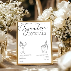 May include: A framed sign with the words "Signature Cocktails" in elegant script. The sign features illustrations of two cocktails, with their ingredients listed below. The sign is surrounded by white flowers.
