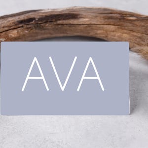 Puede incluir: Un letrero de madera hecho a mano con la palabra "Bienvenido" en una fuente juguetona. El letrero está pintado de blanco con un acabado envejecido y presenta un diseño floral en tonos rosas y verdes. Mide aproximadamente 30 cm de ancho.