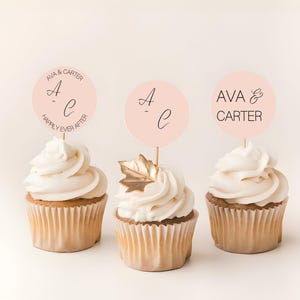 May include: Three cupcakes with white frosting and decorative toppers. The toppers are light pink circles with the names "Ava & Carter" and initials. One cupcake has a gold leaf decoration.