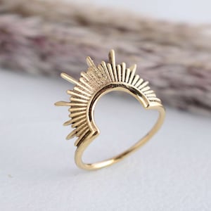 May include: A gold-toned ring with a sunburst design. The ring is open in the back and has a smooth, rounded band.