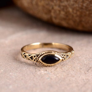 Op de afbeelding: Een gouden ring met een ovale zwarte steen gezet in een decoratieve band.