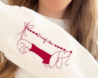 Puede incluir: Sudadera blanca de manga larga con una ilustración roja de dachshund en la manga. El dachshund lleva un vestido rojo y sostiene una cadena de corazones que dice "I Wof You".