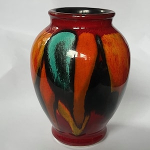 Könnte beinhalten: Eine dekorative Keramikvase mit glänzendem Finish. Die Vase hat eine lebendige Farbpalette aus Rot, Orange, Schwarz und Türkis. Die Vase hat einen abgerundeten Körper und einen schmalen Hals, geeignet zum Präsentieren von Blumen oder als dekoratives Stück.