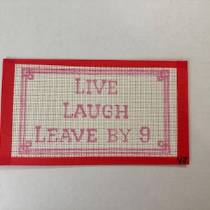 Puede incluir: Un lienzo rectangular de punto de aguja con un borde rojo y las palabras "LIVE LAUGH LEAVE BY 9" en rosa. El texto está centrado dentro de un marco decorativo rosa sobre un fondo crema.