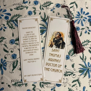 May include: Two bookmarks with a watercolor illustration of Saint Thomas Aquinas. The bookmark on the left has a prayer for wisdom and the bookmark on the right has the title "Saint Thomas Aquinas, Doctor of the Church".