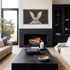 May include: A black framed print of a rabbit peeking out from behind a dark background. The print is hanging above a black fireplace in a modern living room.