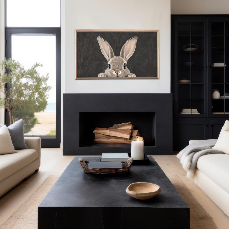 May include: A black framed print of a rabbit peeking out from behind a dark background. The print is hanging above a black fireplace in a modern living room.
