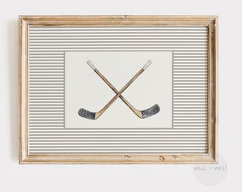 May include: Framed print featuring two crossed hockey sticks. The sticks are brown with black blades and white tape on the handles. The background has a white rectangle with gray stripes, and the frame is a light brown color.