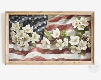 Può includere: Un dipinto incorniciato di un bouquet di fiori bianchi su una bandiera americana piegata. I fiori sono bianchi con foglie verdi e la bandiera è rossa, bianca e blu.