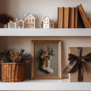 Puede incluir: Una estanter&iacute;a con decoraci&oacute;n navide&ntilde;a. Casitas de cer&aacute;mica blanca con ventanas iluminadas se sit&uacute;an sobre un cuadro enmarcado de un calcet&iacute;n navide&ntilde;o lleno de bastones de caramelo y vegetaci&oacute;n. Tambi&eacute;n hay un regalo envuelto con una cinta marr&oacute;n y una cesta de mimbre.