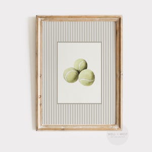 May include: A framed print featuring three tennis balls in a watercolor style. The balls are light green with white accents, set against a white background within a gray border. The frame is a light wood color with a striped gray and white background.
