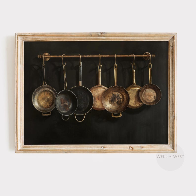 Puede incluir: Una impresi&oacute;n art&iacute;stica enmarcada que muestra siete sartenes de metal variadas colgadas de una barra horizontal sobre un fondo negro s&oacute;lido. Las sartenes var&iacute;an en tama&ntilde;o y acabado met&aacute;lico, desde lat&oacute;n pulido hasta hierro oscuro, todas suspendidas por ganchos.