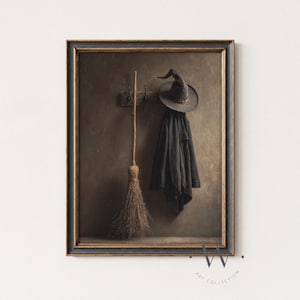 May include: Framed artwork featuring a witch's hat, coat, and broom. The hat and coat hang on a wooden rack, while the broom leans against a wooden shelf. The artwork has a vintage, sepia-toned aesthetic, with a dark frame.