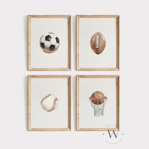 May include: Four framed watercolor prints featuring sports equipment. A soccer ball, football, baseball, and basketball with a hoop are depicted. The prints have a neutral color palette with a white background and wooden frames.