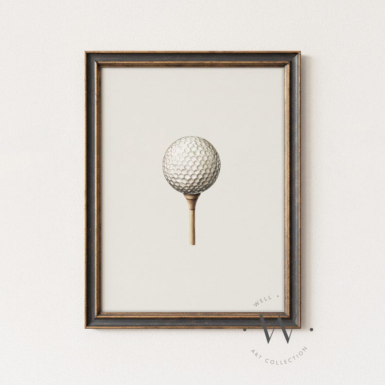 May include: A framed print featuring a golf ball on a tee. The golf ball is white with a dimpled surface, and the tee is a light brown color. The frame is dark with gold accents. The print is from the Well Art Collection.
