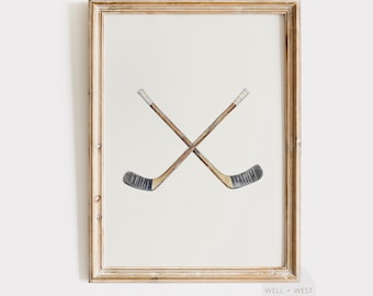 May include: Framed print featuring two crossed hockey sticks. The sticks are brown with black and white details, set against a white background. The frame is a light, natural wood color. The artwork is from the Well + West Art Collection.