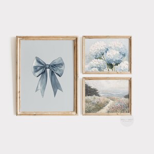 May include: Set of three framed art prints. The top right print features a cluster of blue hydrangeas. The bottom right print depicts a coastal scene with a path. The left print shows a blue bow on a light blue background.