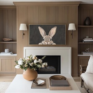 May include: A framed print of a brown rabbit peeking out from behind a dark gray background. The print is hanging on a wall above a fireplace in a living room.