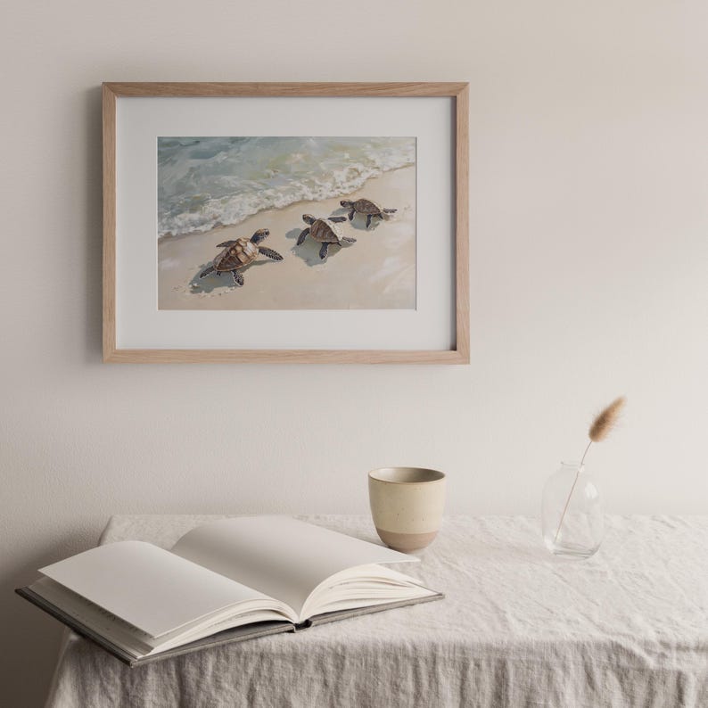 Op de afbeelding: Een ingelijst aquarel schilderij van drie zeeschildpadden die op een zandstrand lopen met oceaan golven op de achtergrond.