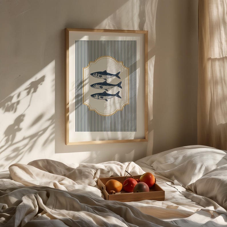 May include: A framed art print showing three blue fish on a cream background, set against navy and white vertical stripes. The print is in a light wood frame, creating a nautical theme. The print is in a light wood frame.