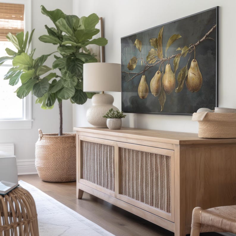 Puede incluir: Una mesa consola de madera clara con dos puertas de armario de mimbre tejido, rematada con una l&aacute;mpara de mesa beige y una peque&ntilde;a suculenta en maceta. Sobre la mesa cuelga un cuadro horizontal de cuatro peras amarillas en una rama oscura.