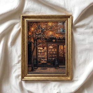 Può includere: Una stampa incorniciata di un'accogliente scena di book café. L'opera presenta un albero con foglie arancioni e luci a stringa, un caffè con libri, tavoli e sedie. La cornice è dorata.