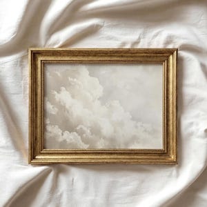 May include: A rectangular framed print featuring a cloudy sky scene. The frame is gold-colored with a detailed, ornate design. The artwork depicts a soft, neutral-toned sky with fluffy white clouds.