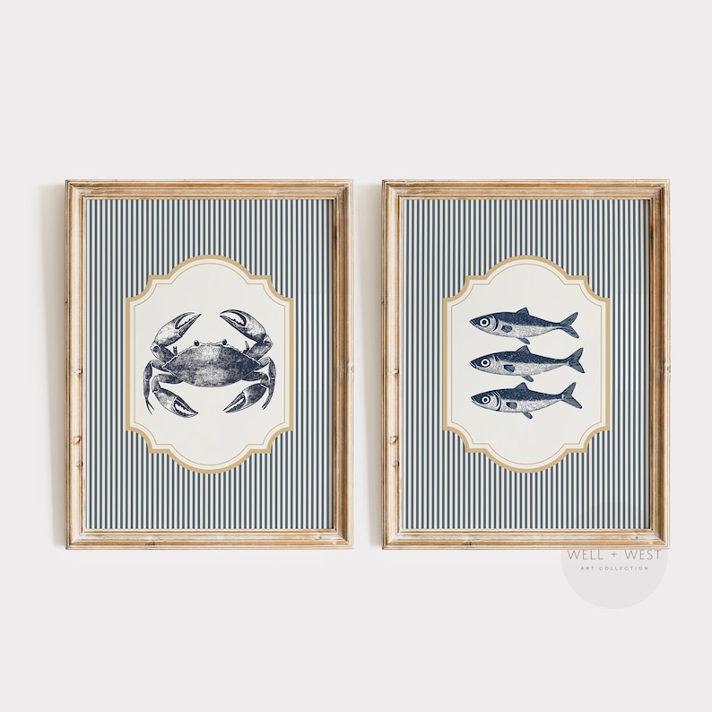 May include: Two framed nautical art prints. One features a detailed crab illustration, the other showcases three fish. Both are set against a blue and white striped background, with a cream-coloured, ornate border and a wooden frame.