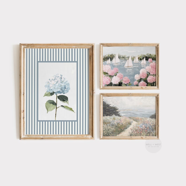 May include: Set of three framed art prints. The prints feature watercolor paintings of a blue hydrangea, sailboats on a lake surrounded by pink flowers, and a coastal path. The frames are a light wood color.