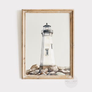 Peut inclure: Peinture à l'aquarelle d'un phare blanc avec une lanterne noire, posé sur une base rocheuse. L'œuvre est encadrée dans un cadre en bois brun clair. Le phare a deux petites fenêtres et se détache sur un fond neutre.