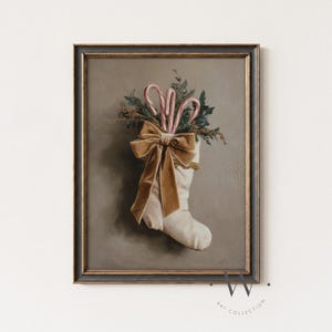 Puede incluir: Impresi&oacute;n enmarcada de estilo vintage que presenta un calcet&iacute;n navide&ntilde;o blanco lleno de vegetaci&oacute;n y bastones de caramelo. Un gran lazo de terciopelo dorado adorna el calcet&iacute;n. La obra de arte tiene una paleta de colores apagados y una est&eacute;tica cl&aacute;sica y antigua.