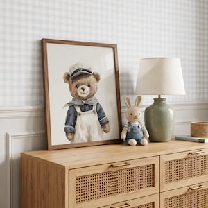 May include: A framed wall art print featuring a watercolor illustration of a brown teddy bear dressed as a sailor in a white cap, blue shirt, and white overalls. The bear has a friendly expression and is positioned next to a small stuffed rabbit.