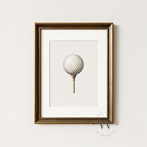 May include: Framed print featuring a golf ball on a tee. The golf ball is white with a dimpled surface, and the tee is a light brown color. The artwork is set against a neutral background and framed in a dark brown wooden frame.