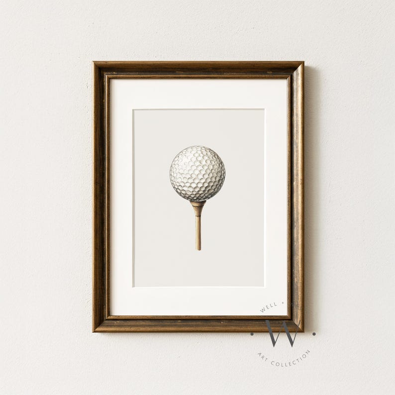 May include: Framed print featuring a golf ball on a tee. The golf ball is white with a dimpled surface, and the tee is a light brown color. The artwork is set against a neutral background and framed in a dark brown wooden frame.