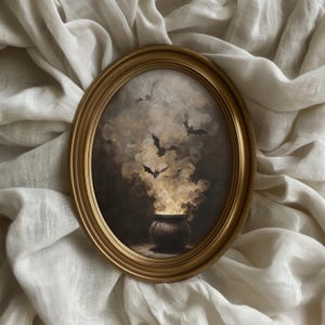 May include: An oval painting in a gold frame. The artwork shows a cauldron with smoke and bats. The painting has a dark, gothic theme, with a focus on Halloween. The frame is gold-coloured.